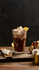A glass of hot chocolate with white marshmallow pieces on a wooden table
