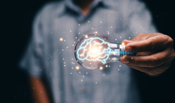 Intelligence and creativity concept. Human holding a glowing light bulb with a digital brain inside. Symbolizing creativity, futuristic innovation, idea generation and modern technology connections. - Powered by Adobe