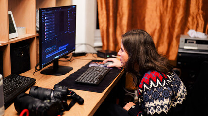 Focused woman working on video and photo editing at home office desk with computer monitor and professional cameras — modern remote work concept