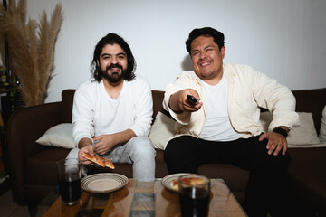 Two Men Laughing and Eating Pizza While Watching TV