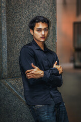 Young Man Leaning Against Wall. A young man in a dark shirt stands confidently against a stone...