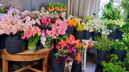 Fototapeta premium Colorful display of fresh flowers arranged in black buckets inside a florist shop. A variety of vibrant blooms pink tulips, roses, white flowers, greenery, and mixed seasonal plants in flower shop