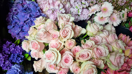Close-up view of assorted fresh flowers in a florist shop, featuring pastel pink roses surrounded by colorful blooms such as hydrangeas, daisies, and tulips