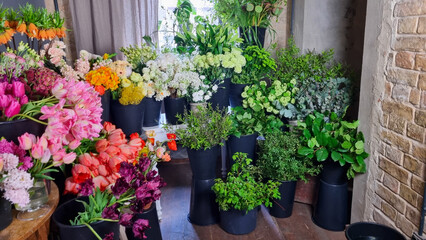 Colorful display of fresh flowers arranged in black buckets inside a florist shop. A variety of vibrant blooms pink tulips, roses, white flowers, greenery, and mixed seasonal plants in flower shop
