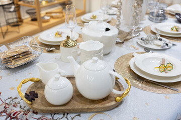 A beautifully set table for a festive event. Two lighted candles, elegant glassware and decorative ornaments are placed near the Christmas tree.