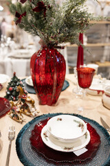 A beautifully set table for a festive event. Two lighted candles, elegant glassware and decorative ornaments are placed near the Christmas tree.