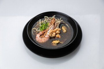 Seafood ramen with prawn, mussels and noodles in soy broth, black bowl on white background