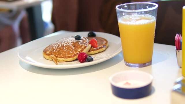 Traditional Eastern European oladyi pancakes presenting golden surface, accompanied by tangy sour cream, vibrant berry sauce, and fresh seasonal berries beside orange juice