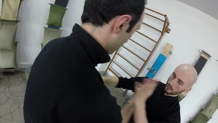 Two professional martial artists wearing black uniforms practicing Wing Chun techniques and self-defense drills together inside a white training studio.

 - Powered by Adobe