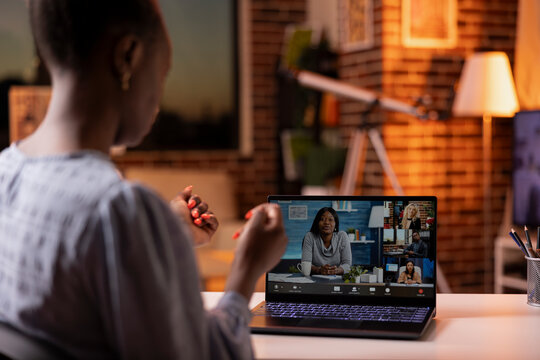 African American female manager leading virtual team discussion on laptop from cozy home during sunset. Black businesswoman attends video conference call, portraying remote work productivity.