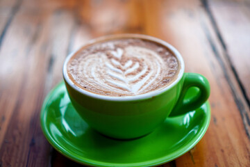 A delightful cup of cappuccino adorned with artistic latte art, served in a vibrant green cup and saucer, resting on a rustic wooden surface, perfect for warm beverage concepts and cafe scenes.