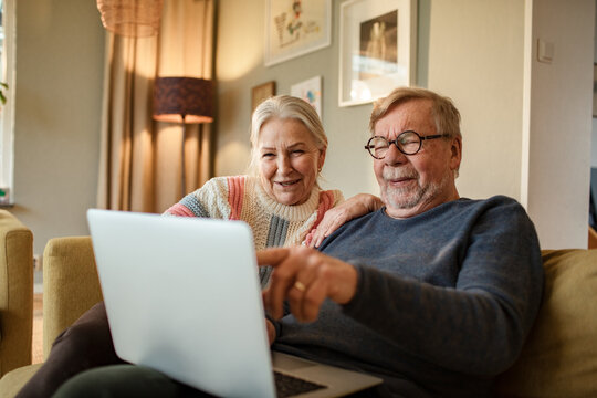 Senior couple smiling while using laptop at home - Powered by Adobe