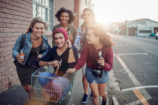 Young adult friends laughing and drinking beer on a city sidewalk