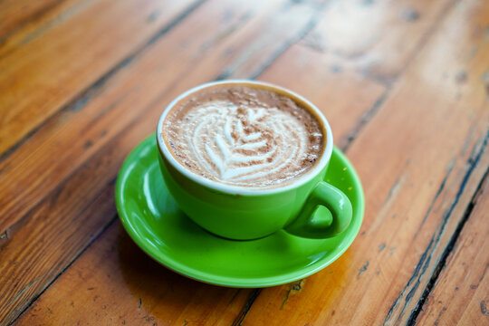 A delicious cappuccino with latte art in a vibrant green cup rests on a rustic wooden table, offering a warm and inviting atmosphere. A perfect pick-me-up for any time of day.
