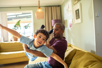 Adult father playing airplane with happy child son in living room