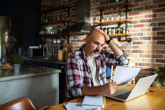 Worried adult man reviewing bills at home kitchen table