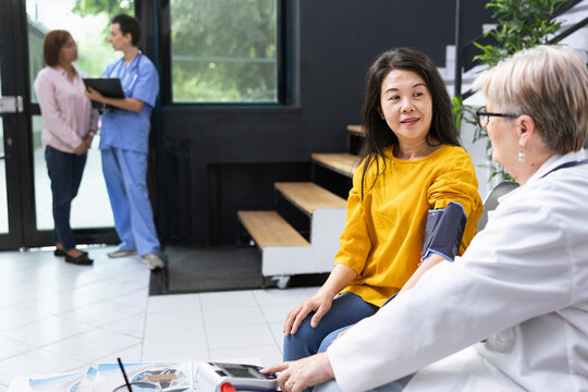 Medical professional performing blood pressure monitoring to asian patient in a hospital waiting area, highlighting health care guidance. BP cuff for checking vitals, accurate pulse reading.