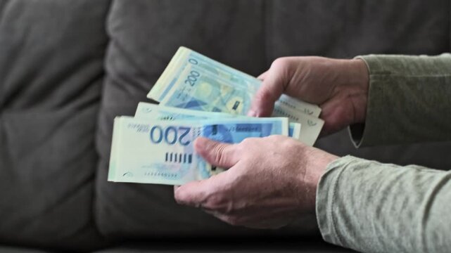 Male hands count Israeli new shekel banknotes in blue color with a 200 NIS denomination in a close-up view