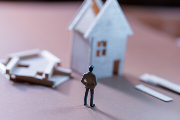 Small figure stands near a partially constructed model house on a simple table