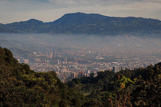 Vista panor&aacute;mica de la ciudad de Medell&iacute;n y Envigado desde la Loma del Escobero, Antioquia, Colombia, con la neblina o poluci&oacute;n flotando sobre el denso valle urbano, enmarcada por monta&ntilde;as verdes.