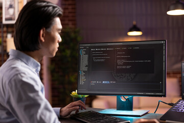 Self employed asian man in apartment home office focusing on coding scripts and software development using computers. Male programmer working remotely to build efficient websites and applications.