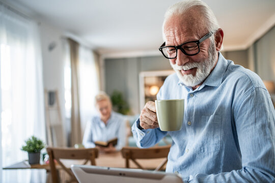 Senior man drinking coffee and using digital tablet at home