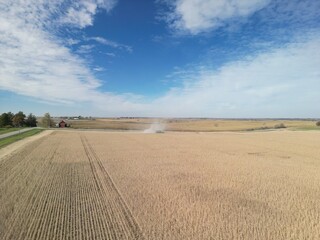 Obraz premium High above the rural Midwest landscapes on a crisp fall day harvest is blowing out lots of dust as the machines make its way down the field bringing in grain. 