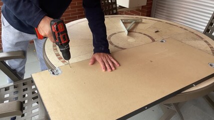 close-up of a man picking up a cordless drill and drilling a hole in a wooden board, home improvement, weekend DIY project