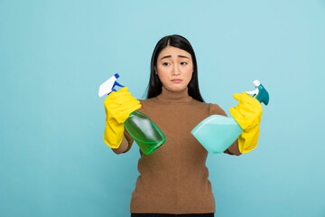 Confused female janitor holding two spray bottles, deciding between detergent solutions. Asian...