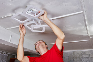 Mounting process involves technician fixing LED chandelier to ceiling during installation task in country home ensuring electrical connection.