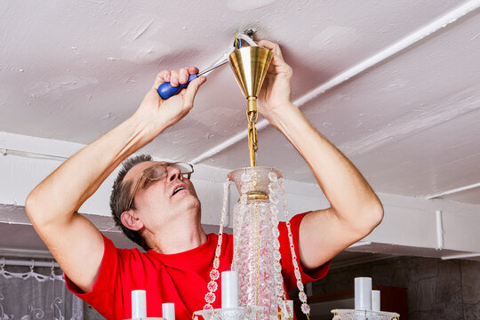 Removing crystal chandelier in country home, individual detaching light fixture from ceiling mount.