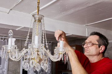 Removal process demonstrates technician taking out bulbs from crystal chandelier before lifting...