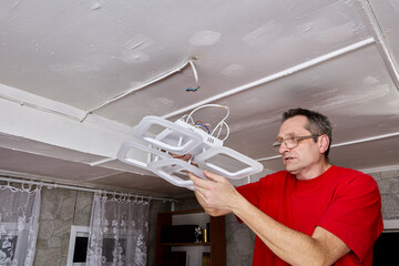 Installation electrician lifts new LED chandelier toward ceiling, exposed wiring visible, fixture...
