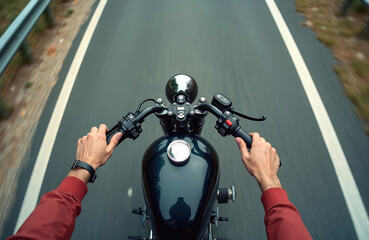 POV shot of person riding black vintage motorcycle on empty asphalt road. Focus on hands gripping handlebars, blurred motion effect adds sense of speed and travel. Classic bike journey.