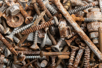 heap of assorted metal fasteners, combining heavily rusted nails and screws with various shiny silver bolts. contrast between the weathered iron oxide and the intact galvanized hardware