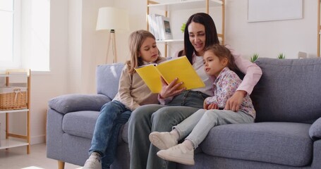 Happy family at home, mother or babysitter holding read book, embrace cute little children daughter, son, parent mum tells small kids funny fairy tale story, sit on sofa having fun together at home - Powered by Adobe