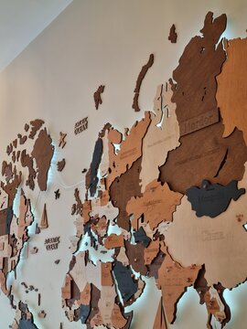 A detailed, illuminated wooden map of the world mounted on a wall, showing continents and countries in various wood tones with engraved names and marked capitals