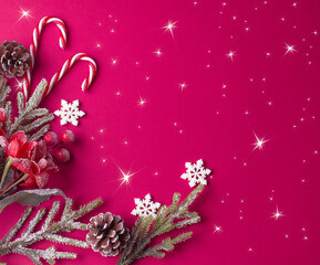 Christmas pink background with decorative poinsettia, fir branch and snowflakes, candy canes and cones for tree decoraton. Winter holiday composition with decor, shiny stars and copy space, top view.