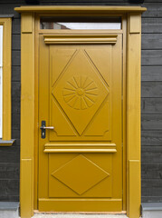 A replica of a historic wooden door, painted mustard yellow with geometric decorative panels and a...