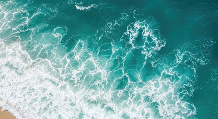 Aerial view of foamy turquoise waves crashing onto a sandy shore. Water's textures & colors are captivating and vibrant