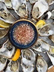 A platter of fresh oysters surrounds a bowl of diced shallots and lemon slices ready for enjoying seafood delicacies.