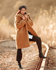 Elegant fashionable lady in brown fur coat over classic business suit on background of country autumn landscape