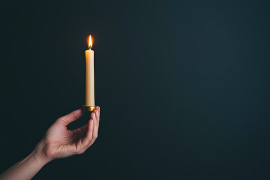 Hand holding a single lit candle on a dark background, representing hope, remembrance, and spiritual vigils