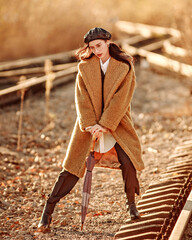 Elegant fashionable lady in brown fur coat over classic business suit on background of country autumn landscape