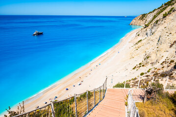 Fototapeta premium Path with stairs to amazing Egremni beach with tuquoise water and anchored boat, Lefkada island, Greece