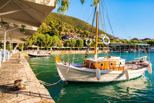Greek taverna tables and traditional wooden fishing boat anchored in Vassiliki port, Lefkada island, Greece
