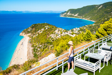 Female tourist looking at stunning Milos beach from high cliff overlooking the Ioanian Sea, Lefkada...