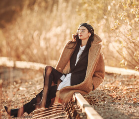 Elegant fashionable lady in brown fur coat over classic business suit on background of country autumn landscape
