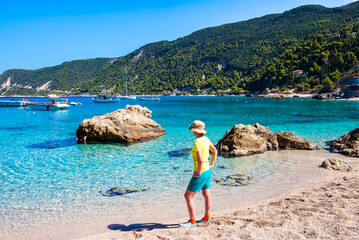 Female tourist standing among rocks and stones with Agios Nikitas beach in background, Lefkada island, Greece