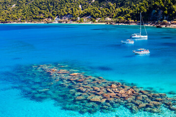 Rocks and stones in crystal clear turquoise sea water of Agios Nikitas bay with sailing boats, Lefkada island, Greece